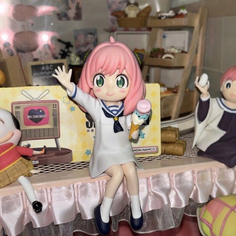 The Anya Forger with Ice Cream Figure from Spy × Family showcases Anya, with iconic pink hair, in a white dress and blue shoes. She enjoys an ice cream cone on a shelf, surrounded by other figurines and a small TV in the background, creating a delightful PVC anime collectible scene.