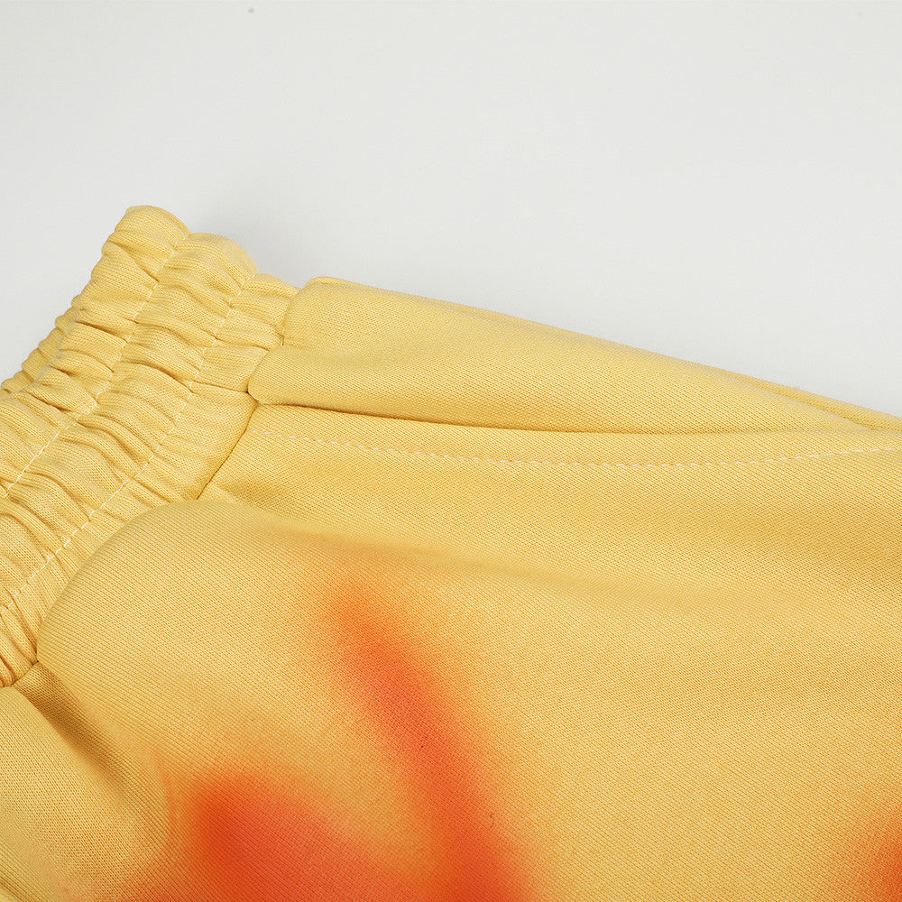 Close-up of yellow sweatpants waistband and side seam with orange spray-dye