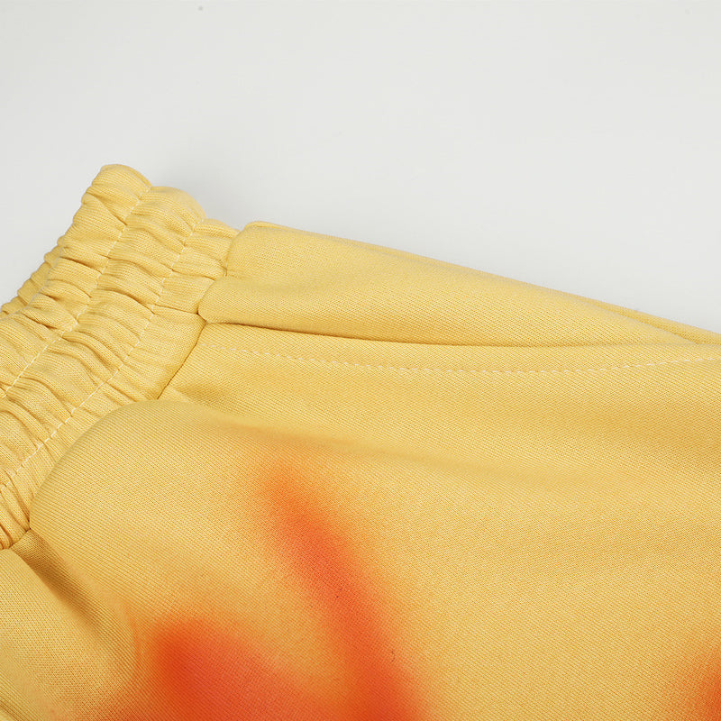 Close-up of yellow sweatpants waistband and side seam with orange spray-dye