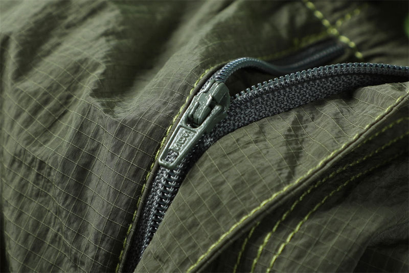 Close-up of a black zipper on crinkled olive fabric with contrasting green stitching