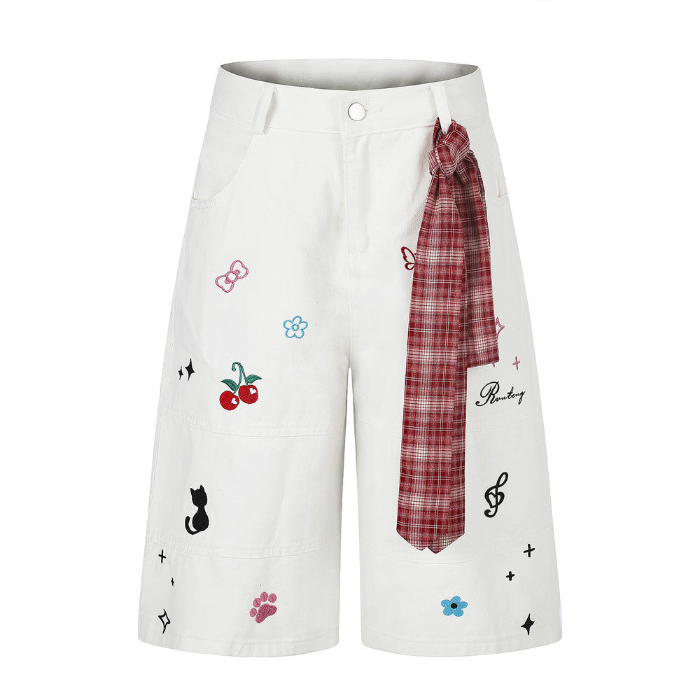 Wide-leg shorts with cartoon embroidery including cherries, black cat, and music notes, featuring a red plaid tie detail at t