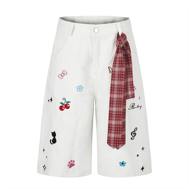 Wide-leg shorts with cartoon embroidery including cherries, black cat, and music notes, featuring a red plaid tie detail at t
