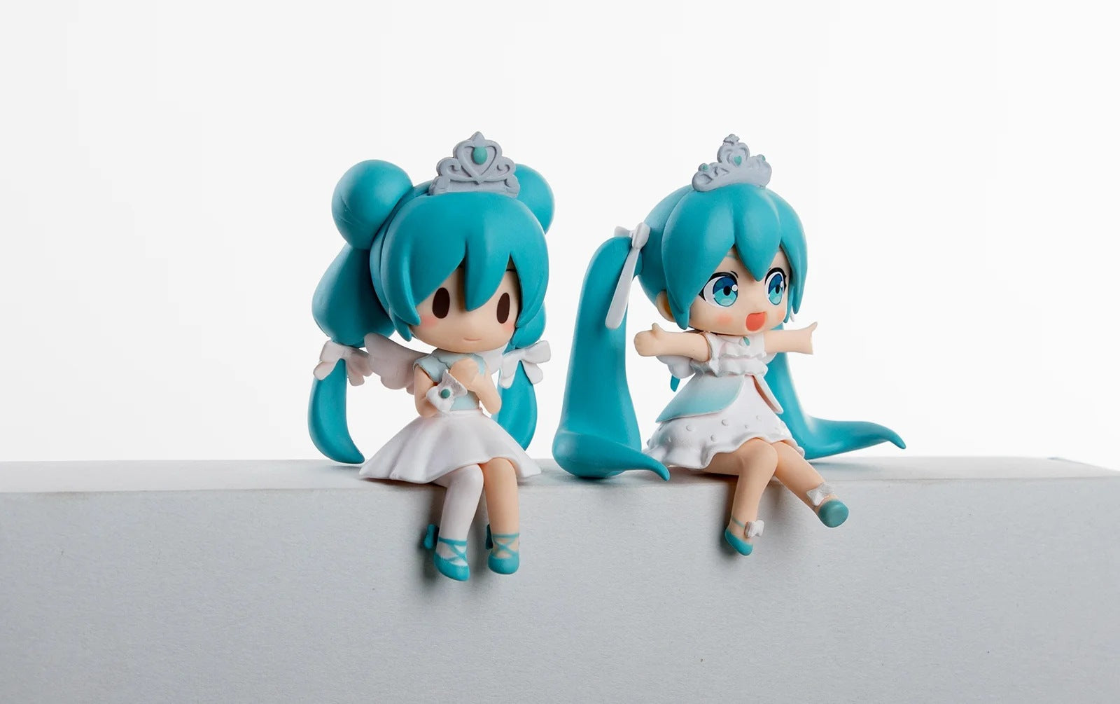 The Hatsune Miku Prayer Hugging Angel Princess 2-piece set features two 7.5cm PVC figures with turquoise hair and white dresses, each with a crown. One has a serene expression, while the other appears excited, all against a plain white background to enhance their ethereal presence.