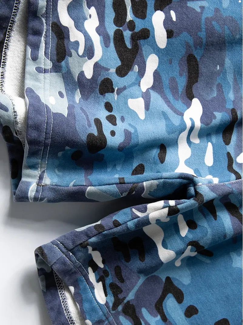 Close-up of blue, black, white, and gray camouflage-patterned cotton fabric from Men's Blue Camo Drawstring Shorts - Relaxed Fit, showing stitched hems and soft inner material.