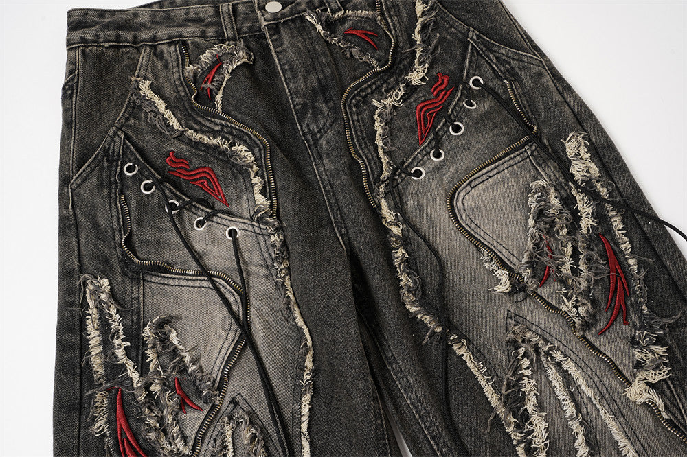 Front view of black patchwork jeans with laced details, frayed seams, and red embroidered accents