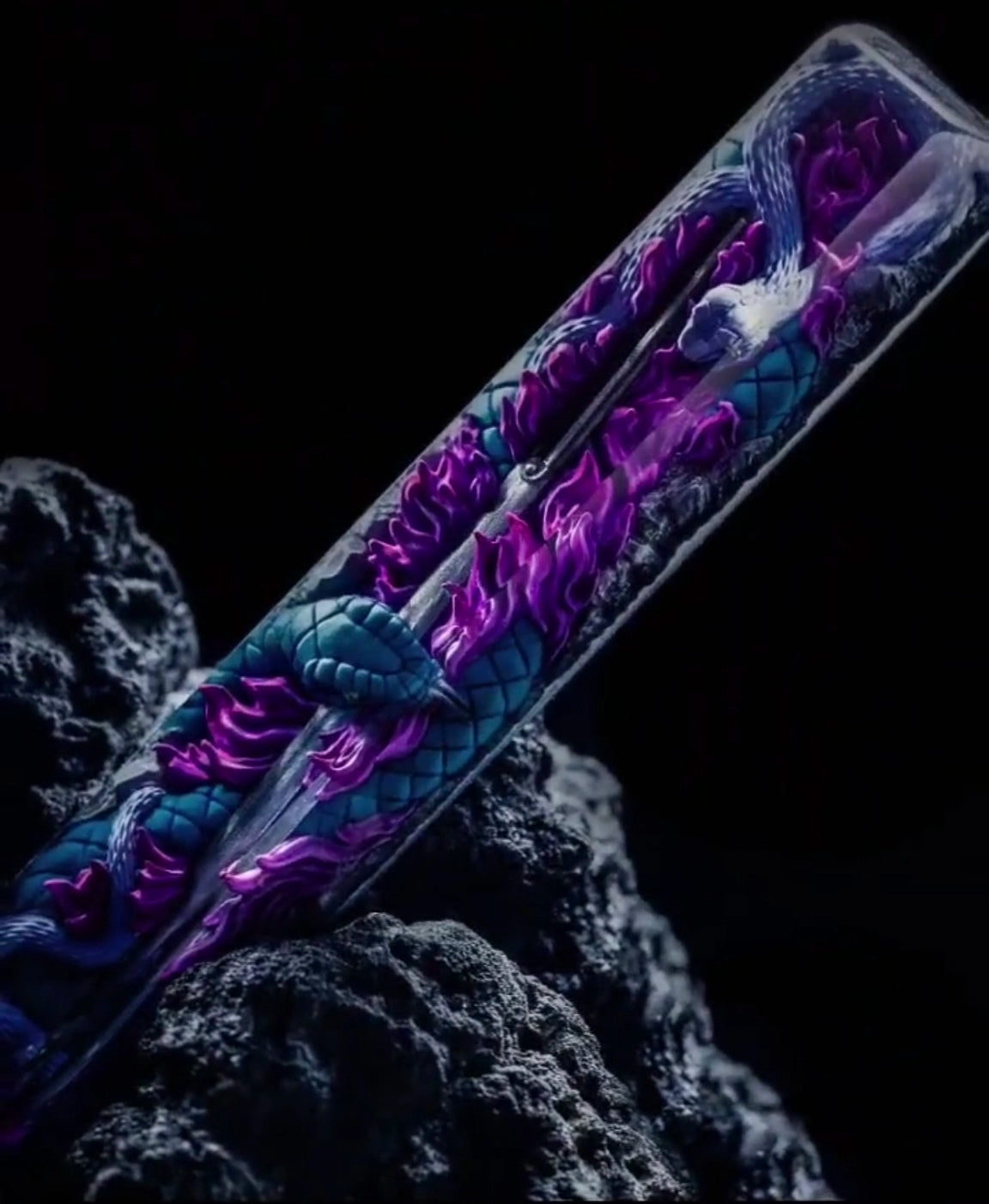 A glass vial with a detailed dragon design in vibrant blue and purple rests on a dark, textured rock. The dragon’s intricately illustrated scales and flowing body resemble the dynamic visuals of Naruto&