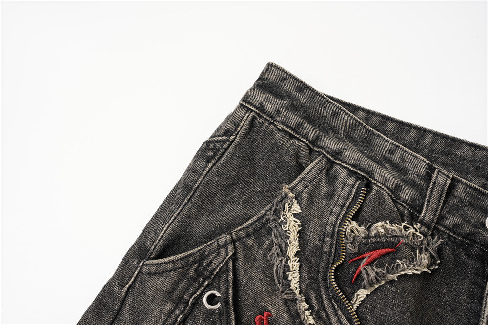 Close-up of the front left waistband and pocket area on distressed black jeans with raw-edge patches