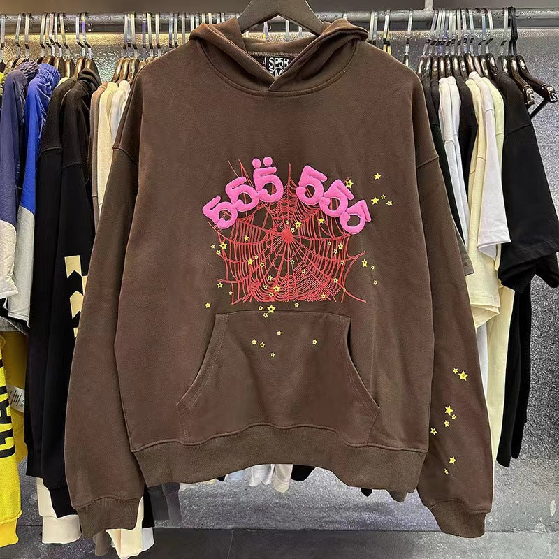 The Stylish Brown Sp5der Hoodie by Sp5der, featuring a trendy web and star print design, showcased among other shirts on a clothing rack, embodies streetwear fashion.