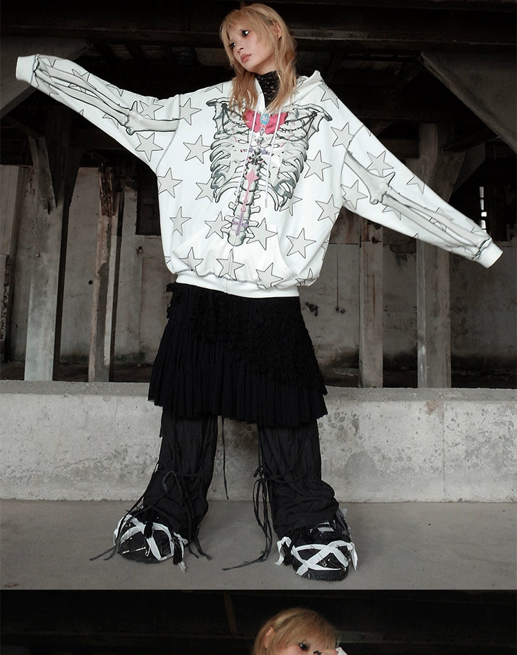 Amidst industrial beams, a person showcases alternative fashion with a Seakoff Gothic Skeleton Star Hoodie – a full-zip hoodie featuring skeleton print and star pattern, paired with a black tiered skirt, black pants, and unique black and white shoes.