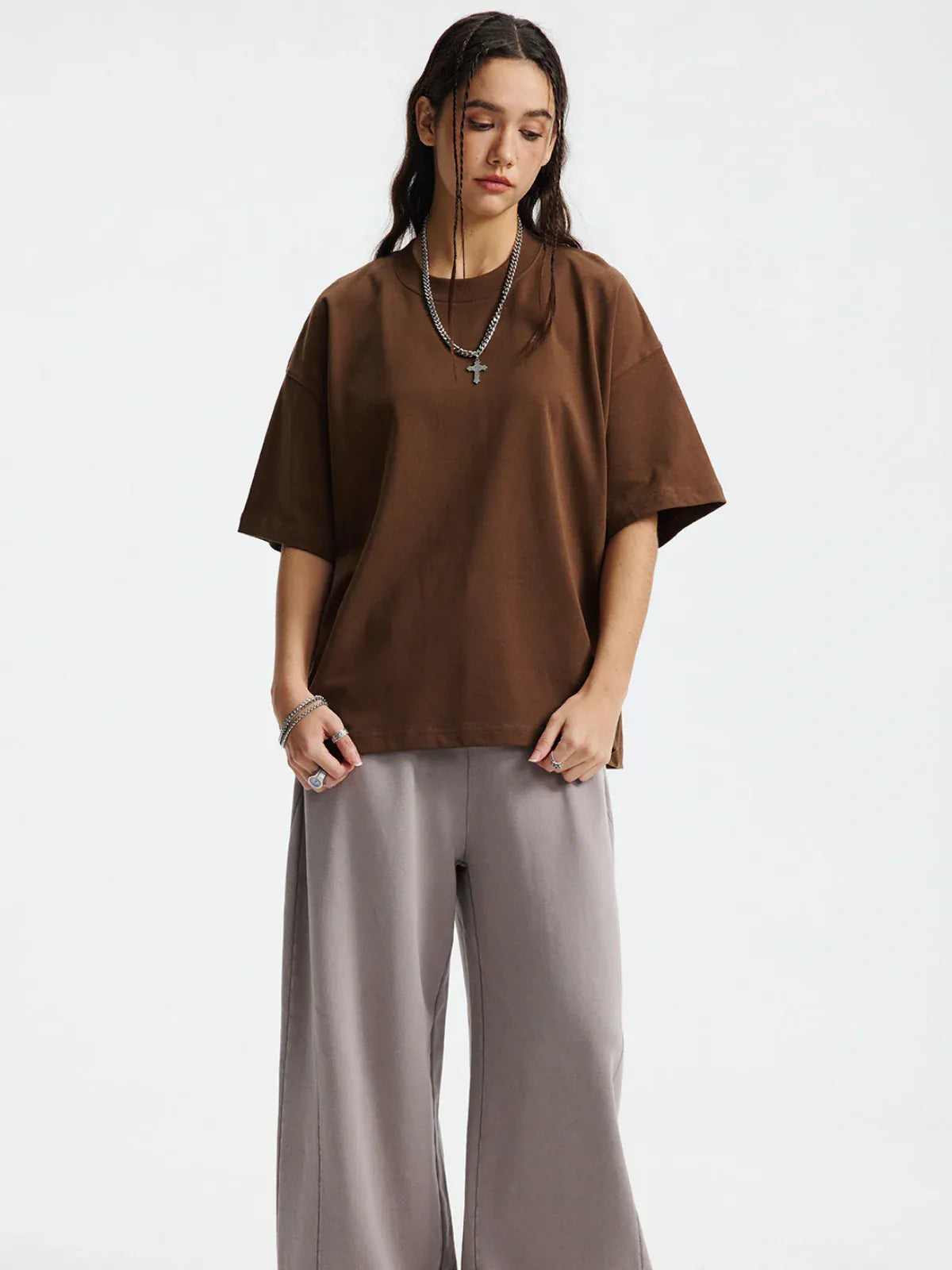 A person stands against a plain white background wearing a Custom Anime Character Chocolate Brown T-Shirt (230GSM 100% cotton, personalized), gray wide-leg pants, and layered necklaces.
