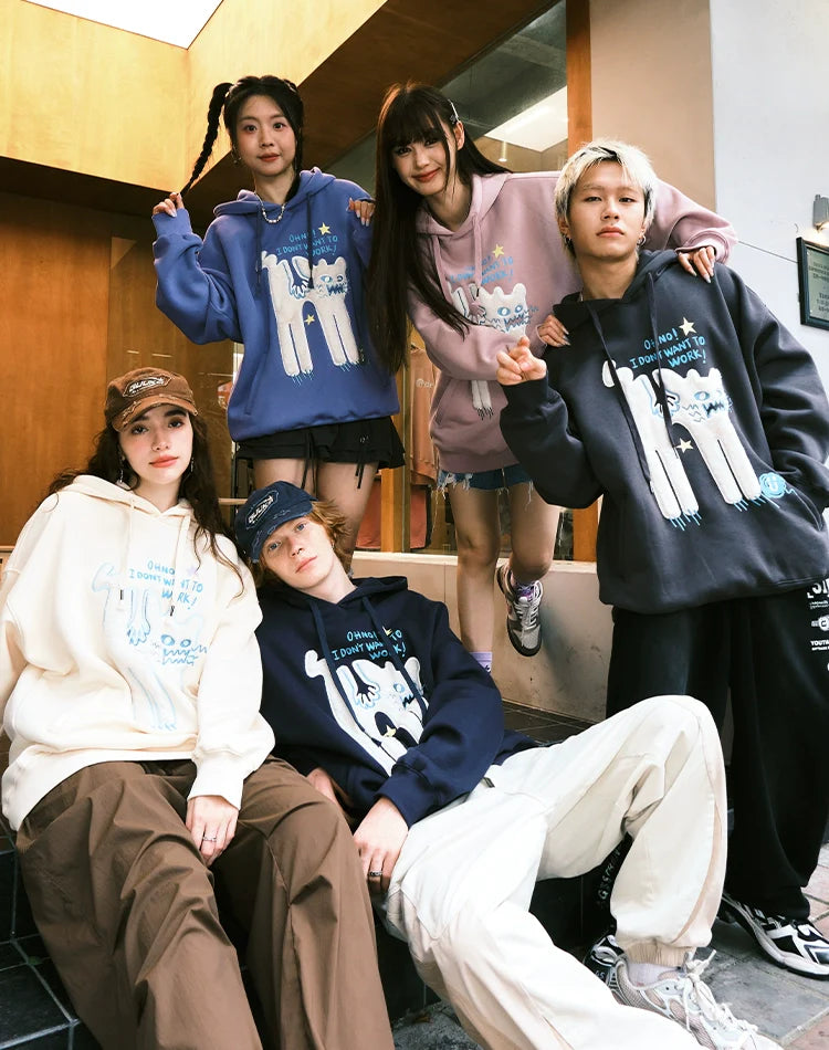 Five people pose casually outdoors on steps, wearing Seakoff's "Oh No! I Don’t Want to Work!" oversized hoodies featuring playful lazy cat graphics, all in front of a wooden door with neutral expressions.