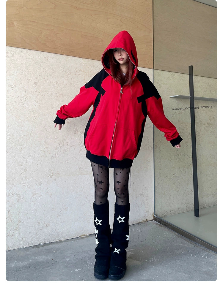 A person poses against a beige wood-paneled wall, wearing the Seakoff Deadpool-Inspired Hoodie—a red and black oversized zip-up superhero sweatshirt—with the hood on, star-patterned tights, and black boots. Their slightly outstretched arms create a bold look as they gaze forward.