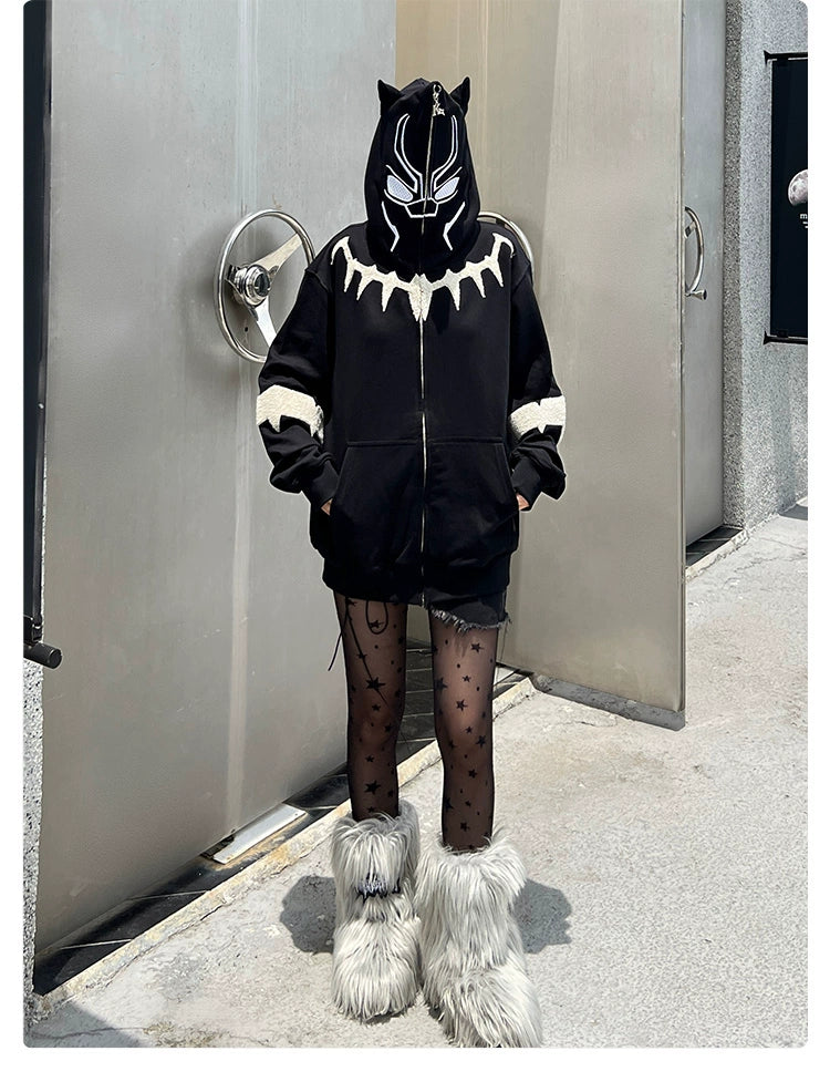 A streetwear icon poses in an urban setting wearing a Seakoff Black Panther-Inspired Hoodie with cat ears, black shorts, star-patterned tights, and oversized fluffy gray boots. The effortlessly stylish scene is framed by metal doors and a concrete backdrop.