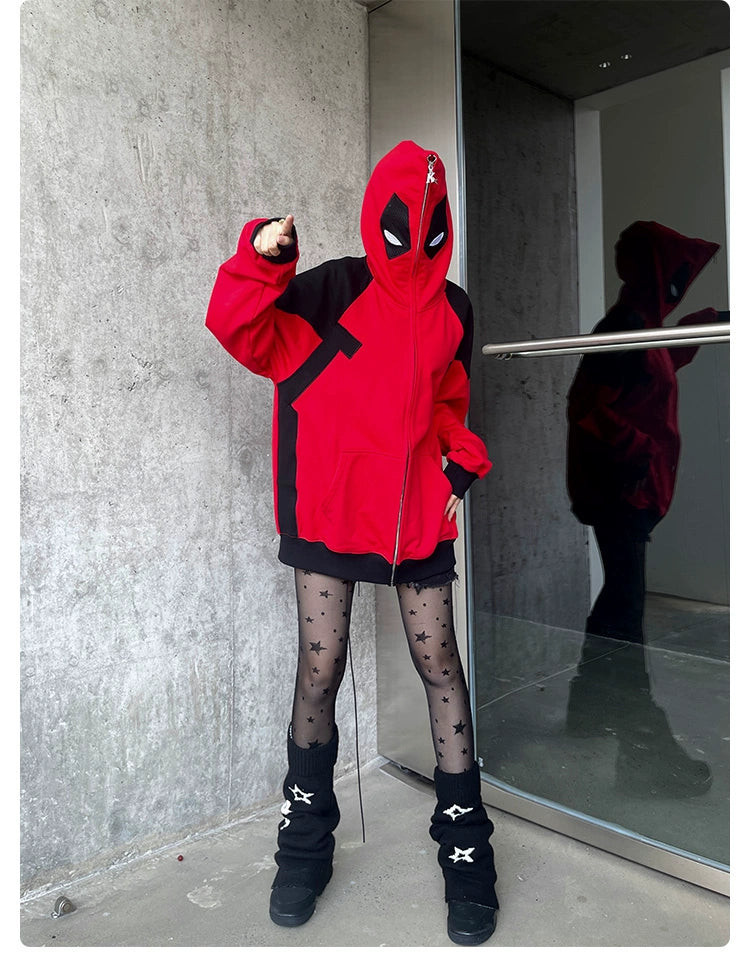 A person wears a Seakoff Deadpool-Inspired Hoodie—an oversized red and black zip-up superhero sweatshirt—paired with a mask. They stand against a concrete wall, adding star-patterned tights and black boots for flair, while their reflection appears in the nearby glass door.