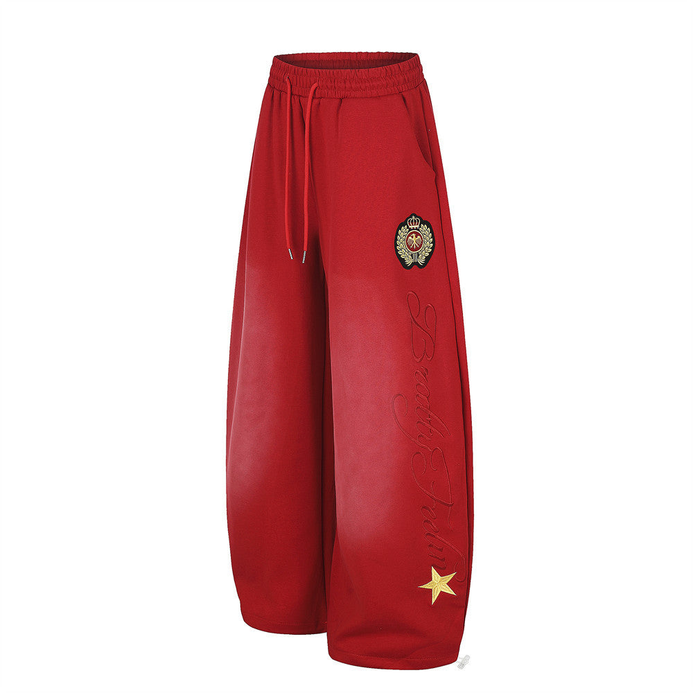 Red wide-leg sweatpants angled front view with crest patch and script embroidery