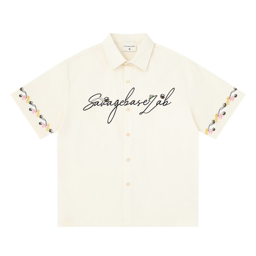 Cream short sleeve button-up shirt front view with script logo and floral embroidered sleeve hems