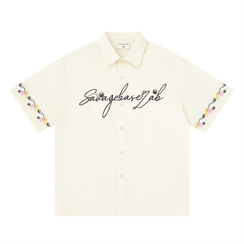 Cream short sleeve button-up shirt front view with script logo and floral embroidered sleeve hems