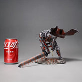 A Berserk Guts Bloodstained Warrior Statue features a knight in detailed armor with a large sword on a rock-like base, wearing a tattered red cape. A red soda can is placed nearby for scale against this imposing 1/7 scale PVC figure. The background is plain gray.