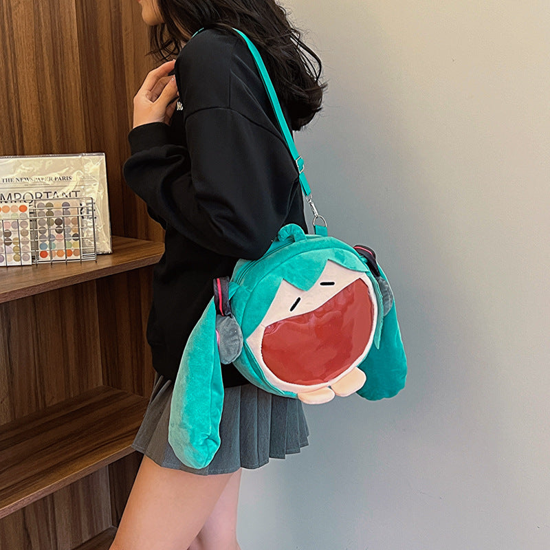 A person wearing a black sweater and gray skirt holds a Seakoff Cute Anime Hatsune Miku Backpack, a plush ita bag with large ears and an open mouth. They stand near wooden shelves displaying anime merch, adding playfulness to the scene.