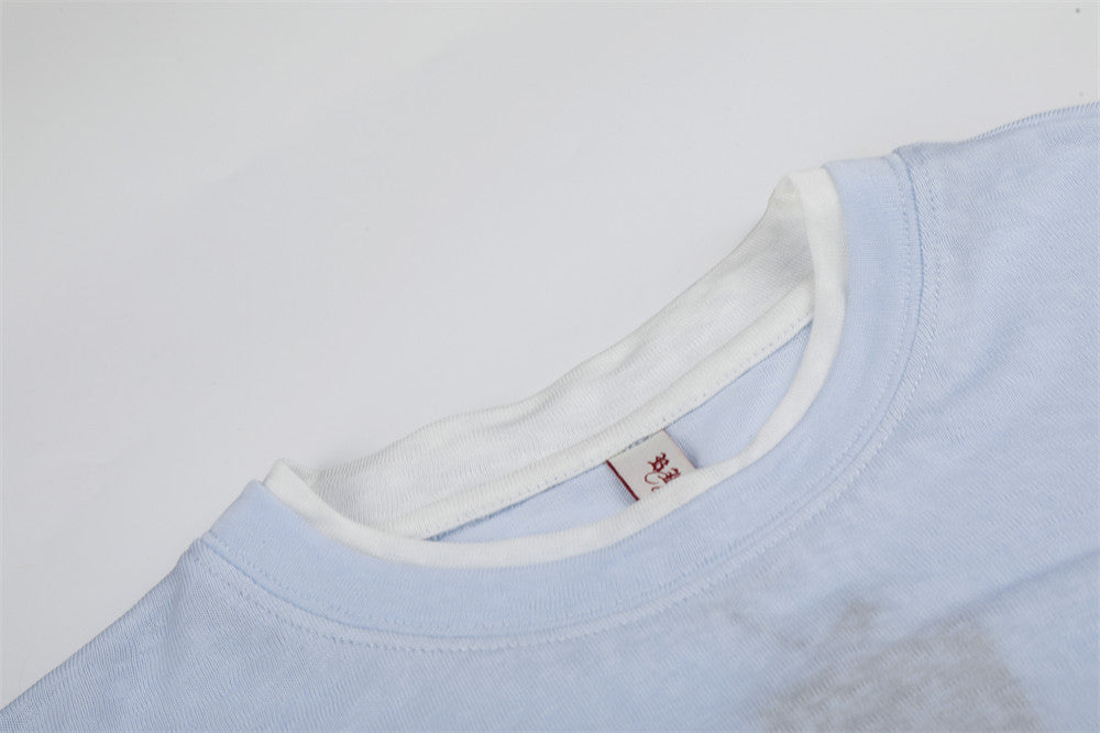 Close-up of white ribbed crew neckline and shoulder seam on light blue tee
