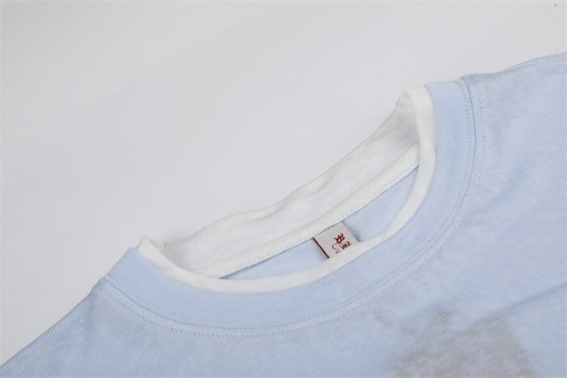 Close-up of white ribbed crew neckline and shoulder seam on light blue tee