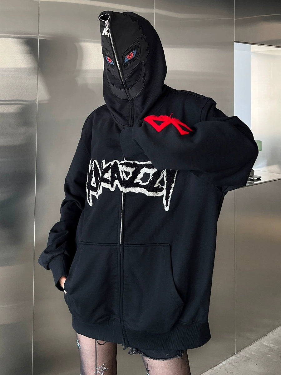 A person in a Berserk-Inspired Griffith Dark Knight Hoodie, a black zip-up oversized streetwear piece with bold white graphics and red sleeve detailing, hides their face with a black mask featuring red eyes against a minimalist metallic wall.