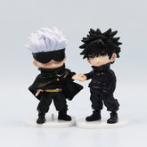 Two chibi-style figures from the Jujutsu Kaisen Q Edition Spell Return 7-Piece PVC Collectible Set feature one with spiky white hair, black sunglasses, and a black outfit holding hands with another in matching attire on white circular bases.