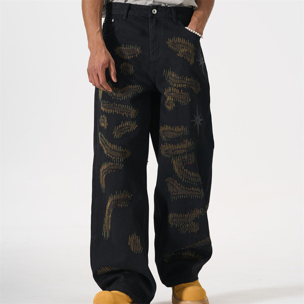 Black wide-leg jeans with all-over chaotic needle embroidery in gold and olive tones and eight-pointed star patches, shown fr