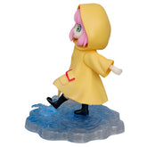 The Anya Forger Yellow Raincoat Figure from Spy × Family features pink hair and a yellow hooded coat. It stands in a water-splash base, with black boots, red buttons, and a belt, capturing the whimsical charm of anime figures.