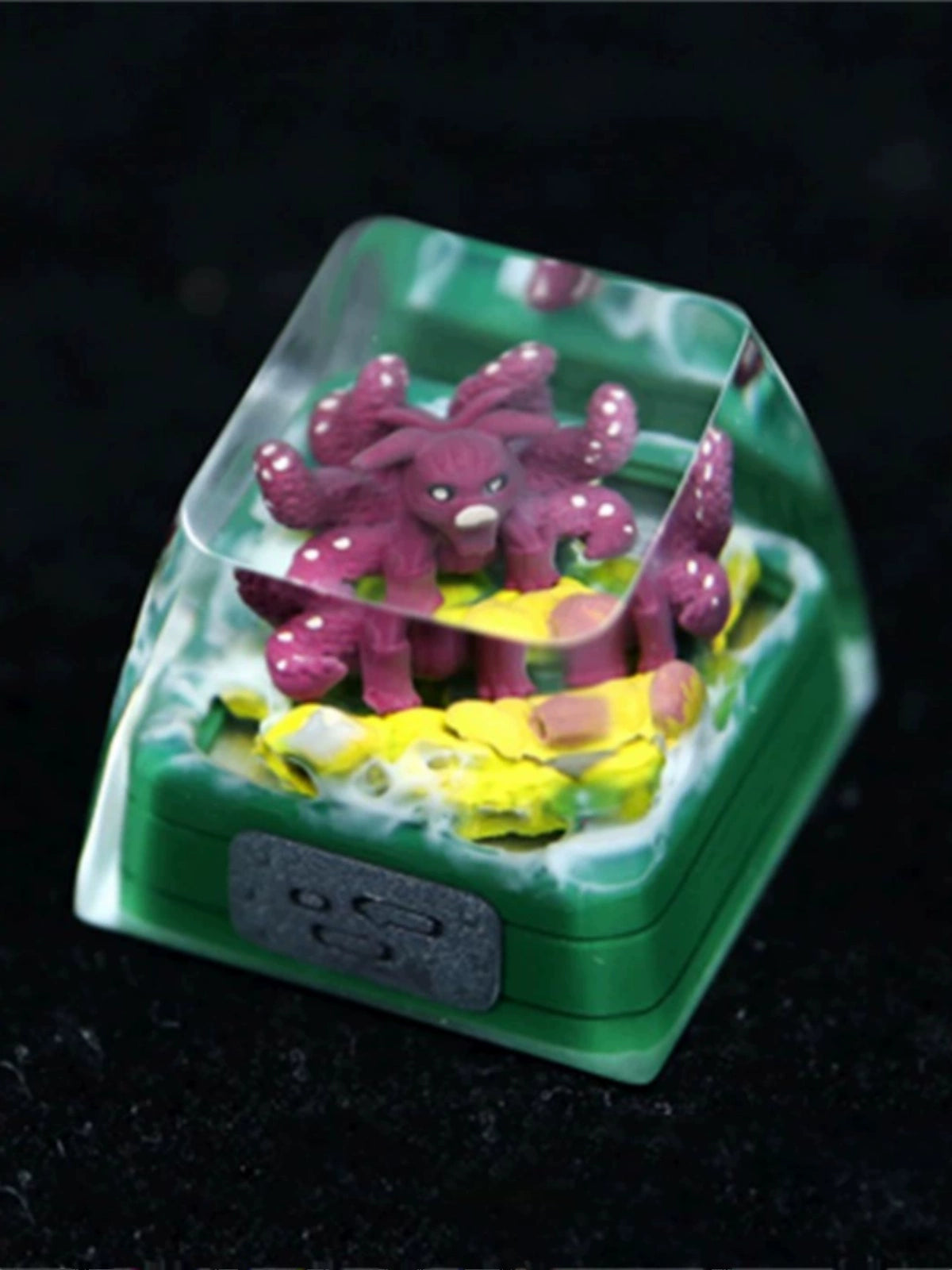 This Naruto Tailed Beasts keycap from the Bijuu collection features a purple octopus with white spots on yellow rocks, encased in a clear resin dome atop a green base, capturing the mystical essence of Kurama, Shukaku, and Saiken.