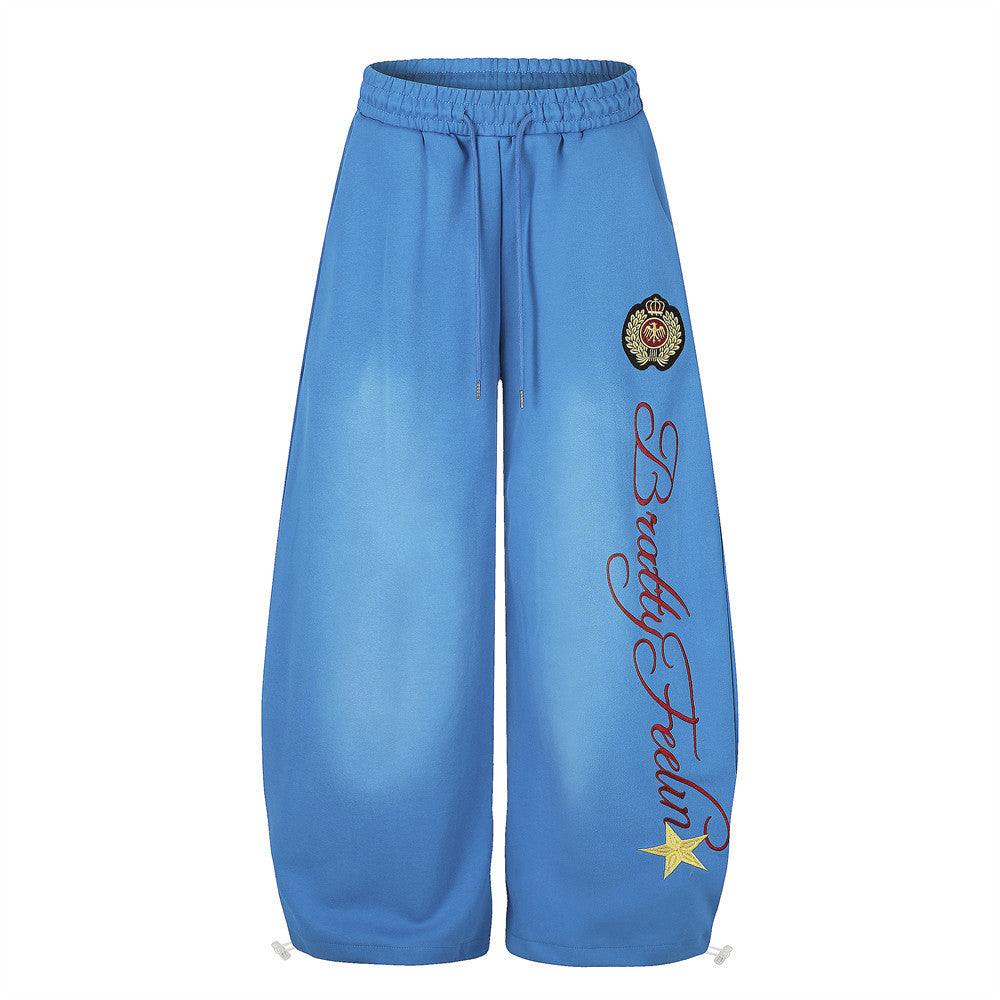 Blue wide-leg sweatpants front view with crest badge, script print, and yellow star