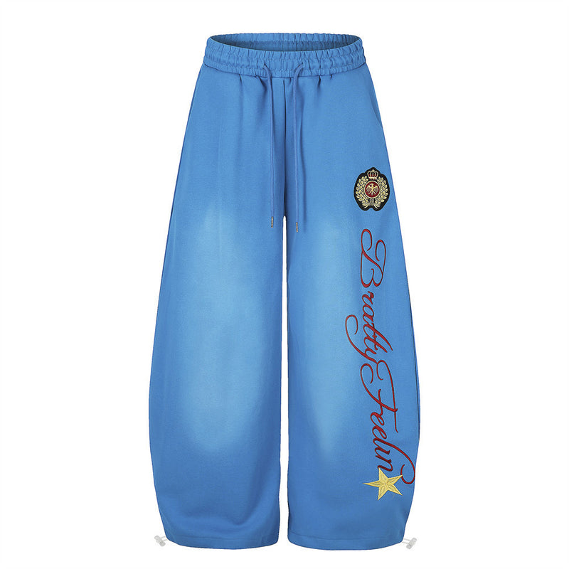 Blue wide-leg sweatpants front view with crest badge, script print, and yellow star