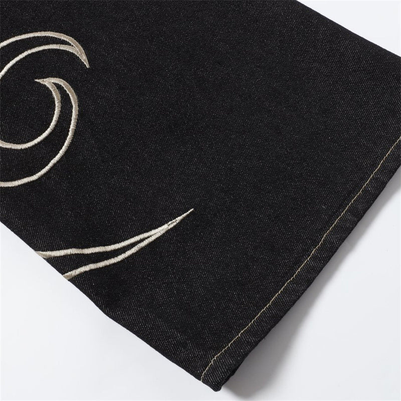 Close-up of black denim hem with embroidered flame detail and tan stitching