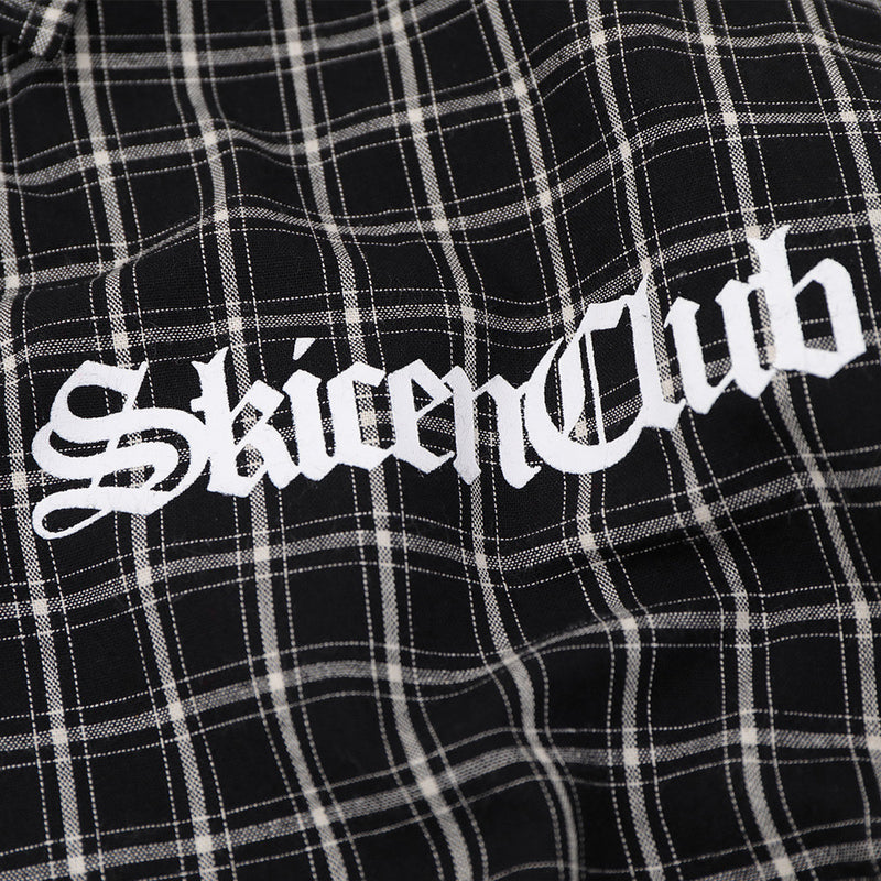 Close-up of white Gothic logo print on black plaid shirt