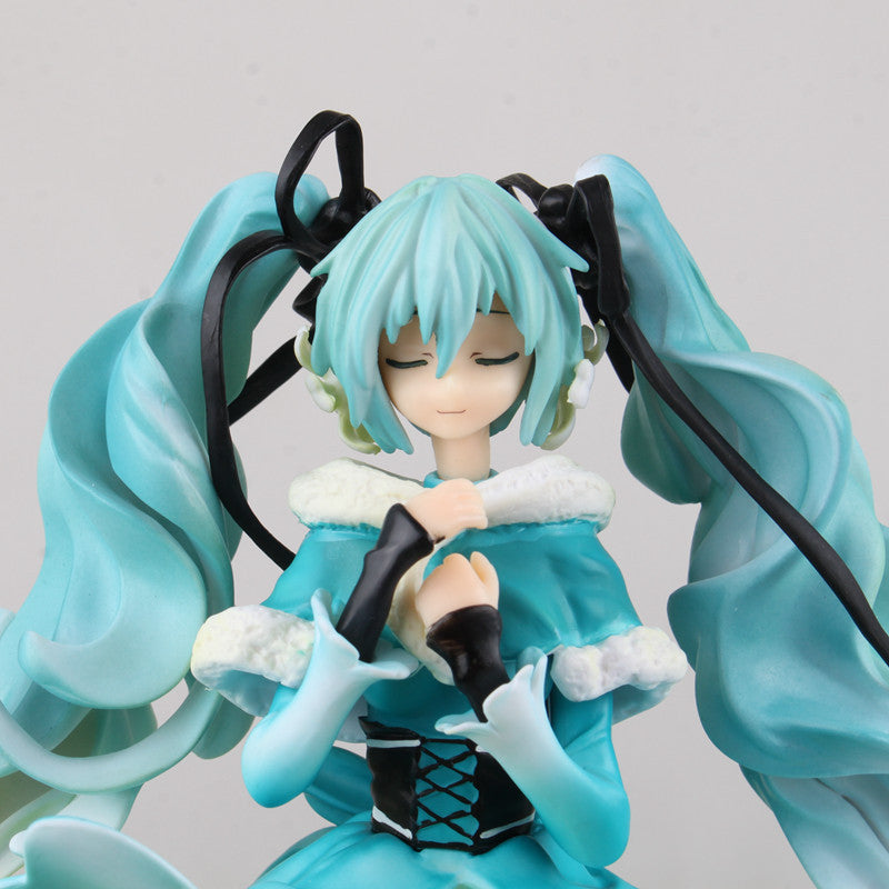 This captivating Hatsune Miku 1/7 scale 28cm PVC figure by Hatsune Miku displays her flowing hair and closed eyes. She wears a teal and white winter-themed outfit with ribbon and fur-trimmed details, posing gracefully with hands clasped at her chest.