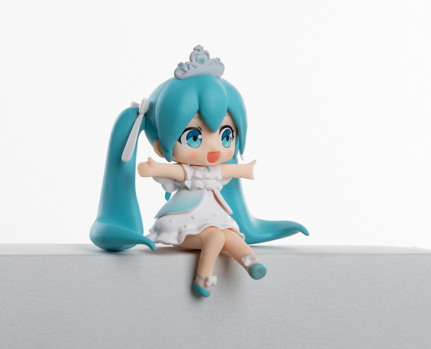 The Hatsune Miku Prayer Hugging Angel Princess 2-piece Set features a 7.5cm PVC figurine with blue hair, long pigtails, a white dress, and crown. She sits on the edge with arms outstretched, legs dangling against the plain white background.