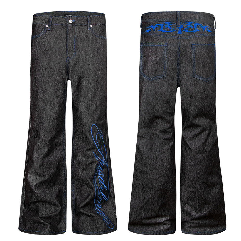 Jean homme noir bootcut évasé en denim brut, broderie cursive bleue sur le bas de la jambe et broderie tribale sur la ceinture arrière