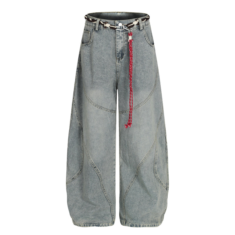 Vaquero de pierna ancha y corte barrel en denim azul claro lavado, con costuras curvas de patchwork deconstruido y cinturón de cuerda trenzada