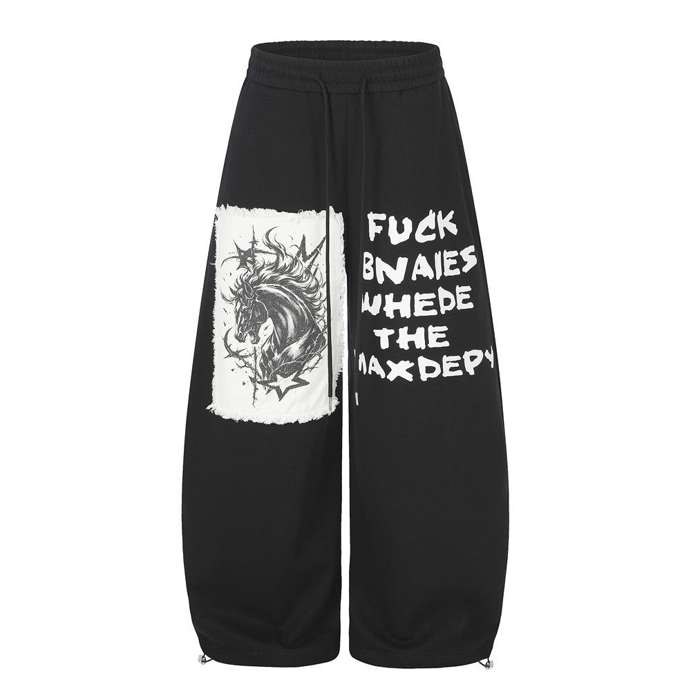 Pantalon de survêtement homme noir à jambes larges, écusson licorne gothique appliqué et grand imprimé slogan sur les empiècements des jambes