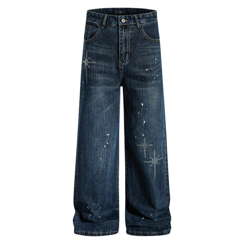 Men's wide-leg washed denim jeans with rhinestone cross motifs and white paint-splatter detail in deep indigo blue