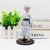 The Jujutsu Kaisen Satoru Gojo PVC Figure is an 18 cm collectible statue of the white-haired, blue-eyed anime character in a light gray yukata with a dark blue belt and black sandals, set on a black circular base near a white wooden fence and green plant.