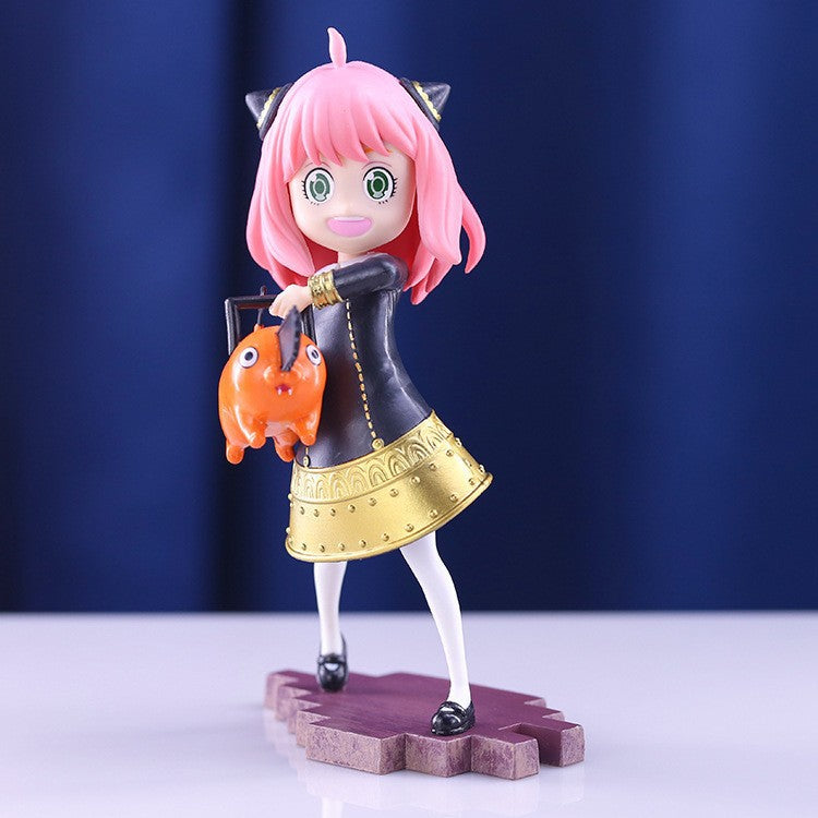 The Anya Forger Chainsaw Cosplay Figure features pink hair, cat ears, a black and gold dress, and holds an orange creature with large eyes. This 18CM PVC Spy x Family Anime Collectible stands on a patterned base with a serene blue backdrop.