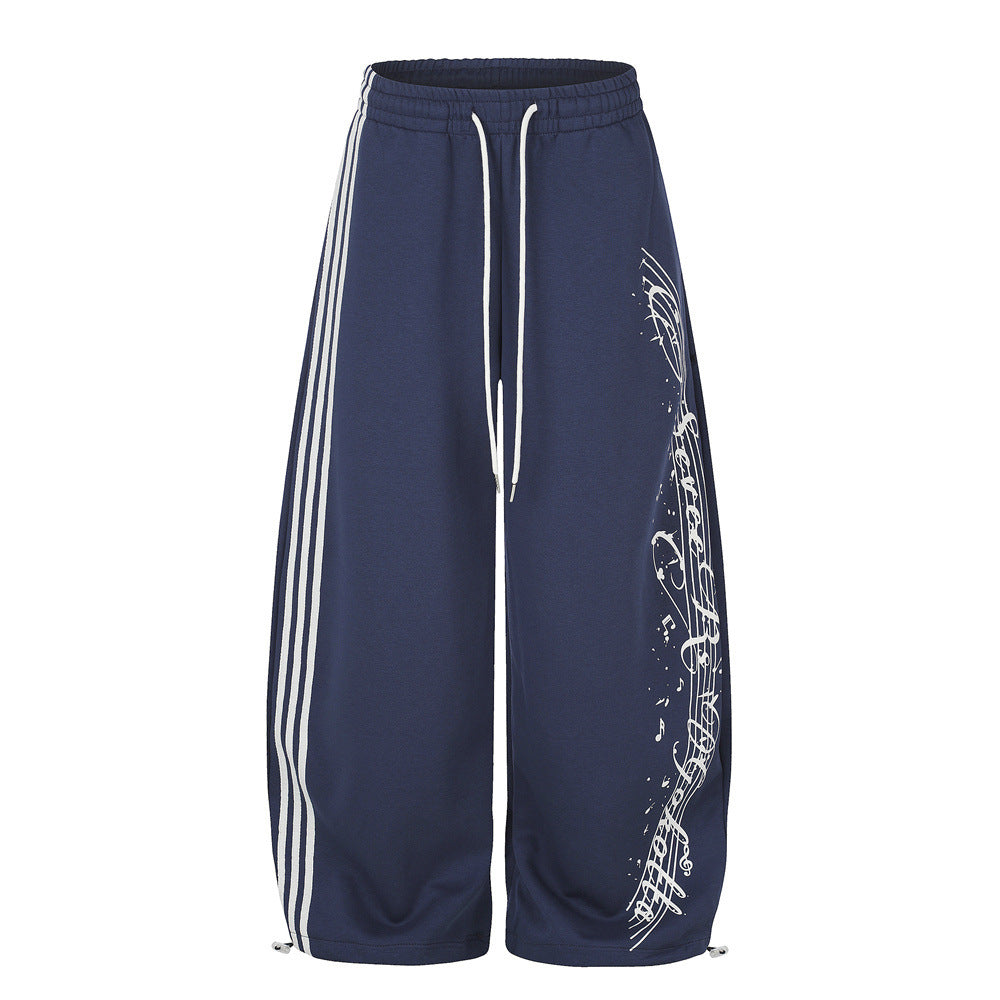 Wide-leg navy sweatpants with three white side stripes and music note script print on the front leg