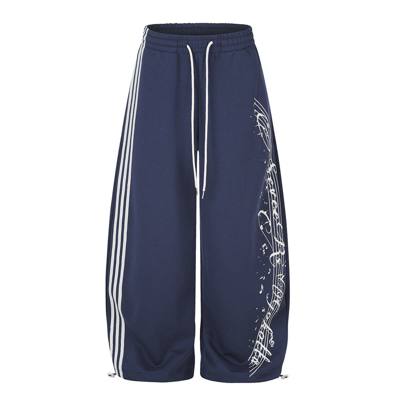 Wide-leg navy sweatpants with three white side stripes and music note script print on the front leg