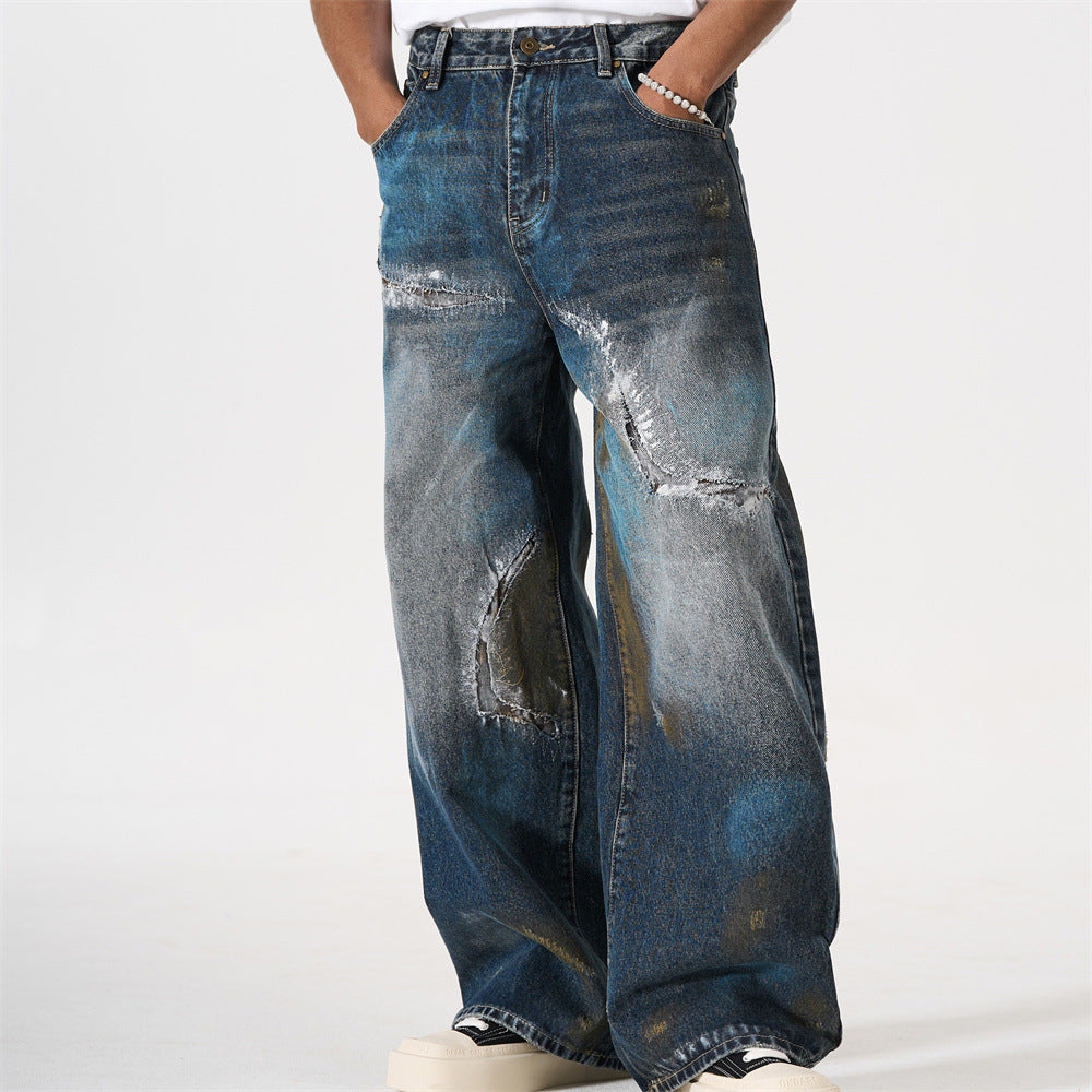 Men's distressed wide-leg jeans with patch repairs, splatter bleach wash, and grunge punk styling in washed indigo denim