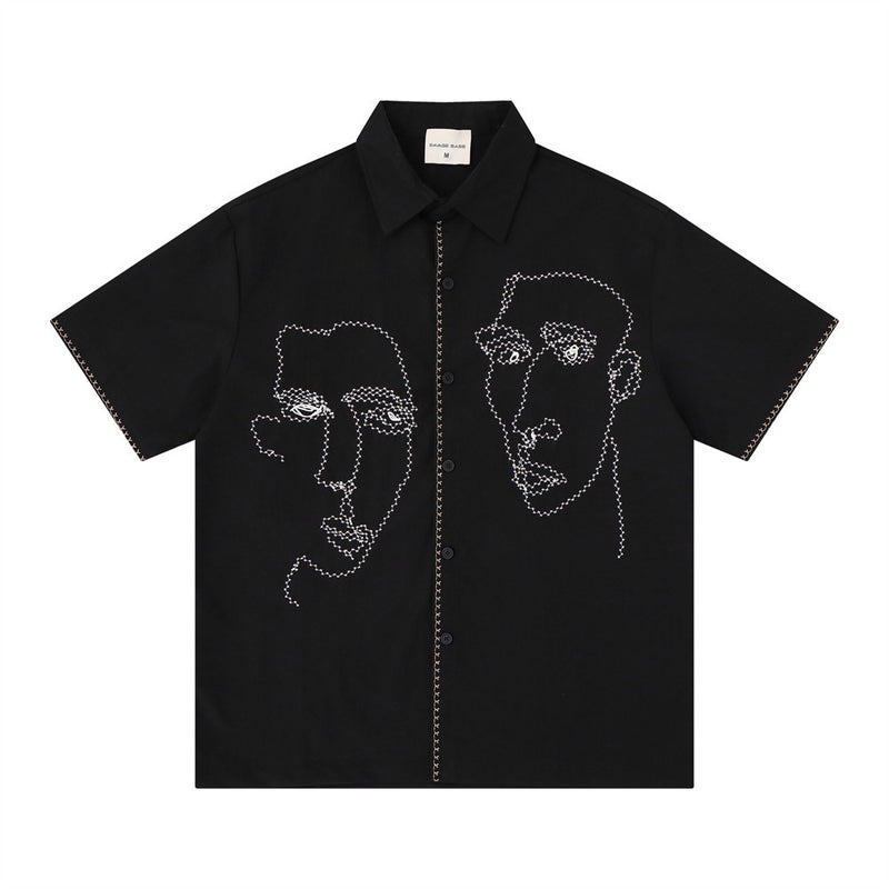 Oversized short-sleeve button-up shirt with abstract face line-art embroidery on front panels, shown in black colorway