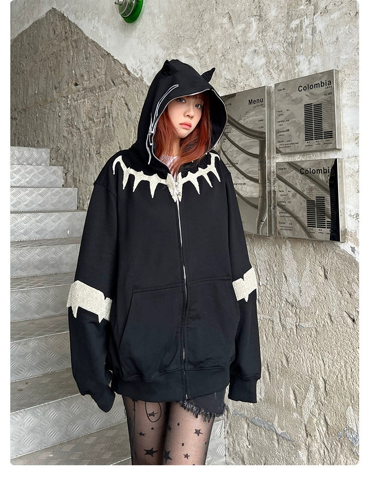 A streetwear fan stands on a staircase, wearing a Seakoff Black Panther-Inspired Hoodie with pointed ears and jagged white designs. The outfit is completed with a black star-patterned sheer skirt, embracing the oversized fit trend.