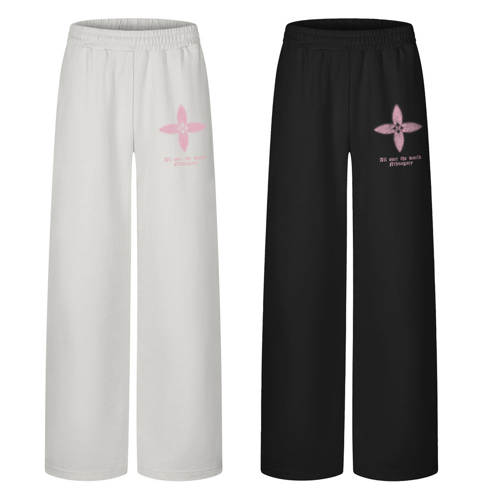 Men's wide-leg sweatpants with four-petal floral graphic print on left thigh, shown in black and gray colorways