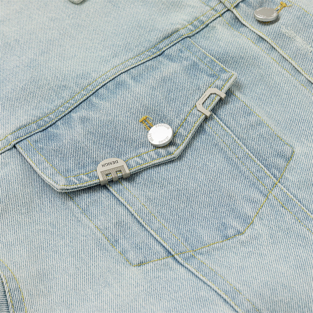 Close-up of a chest pocket flap with silver-tone button and rectangular metal hardware on denim