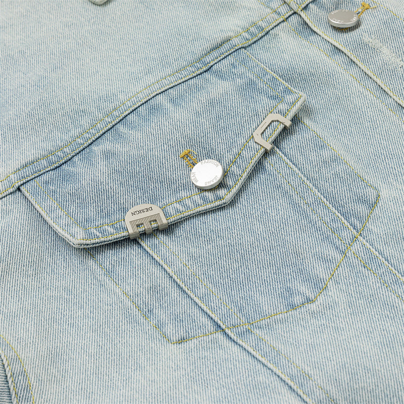 Close-up of a chest pocket flap with silver-tone button and rectangular metal hardware on denim